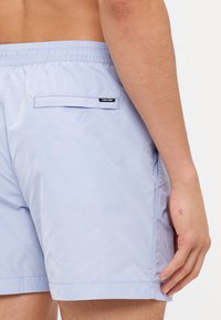 Heledad sinised ujumispüksid, mis on valmistatud siledast kangast, elastse vöökoha, küljetaskute ja väikese musta logoga taga.
