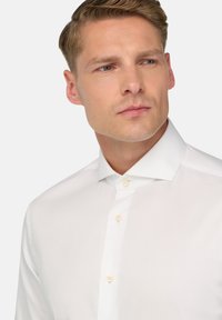Camicia bianca strutturata con colletto classico e quattro bottoni chiari visibili. Messa a fuoco ravvicinata sul colletto e sulla parte superiore del tessuto.