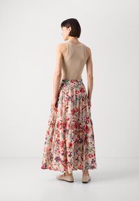 Maxi gonna floreale con un top tank aderente beige. La gonna presenta una vita arricciata e un motivo di fiori rossi, viola e verdi su uno sfondo chiaro.