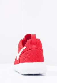 Červená atletická obuv s texturovaným síťovaným svrškem, bílou podrážkou a výrazným bílým logem swoosh. Obsahuje poutko na patě.