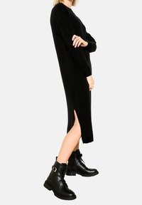 Svart knälång tröjdress med långa ärmar, sidoklyvning och lös passform. Matchad med svarta ankelstövlar med spännen.