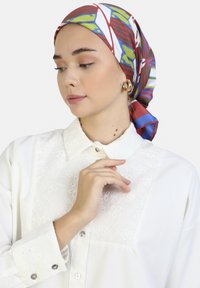 Foulard di seta con audaci motivi rossi, blu e verdi abbinato a una camicia bianca con bottoni caratterizzata da ricami floreali e un colletto classico.