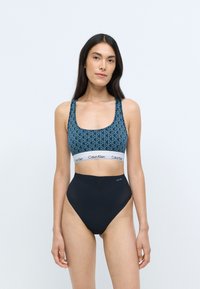 Blå mønstret bikini top med brede stropper og logoelastik, parret med højtaljede sorte bikini underdele med en glat overflade.