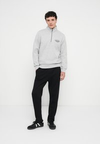 Maglione in pile grigio con mezza cerniera, caratterizzato da un logo sul petto, abbinato a pantaloni della tuta neri e scarpe da ginnastica nere con strisce bianche.