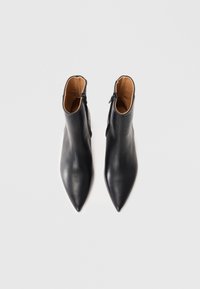 Bottines en cuir noir, à bout pointu, texture lisse, avec des zips latéraux ; intérieur doublé d'un matériau beige.