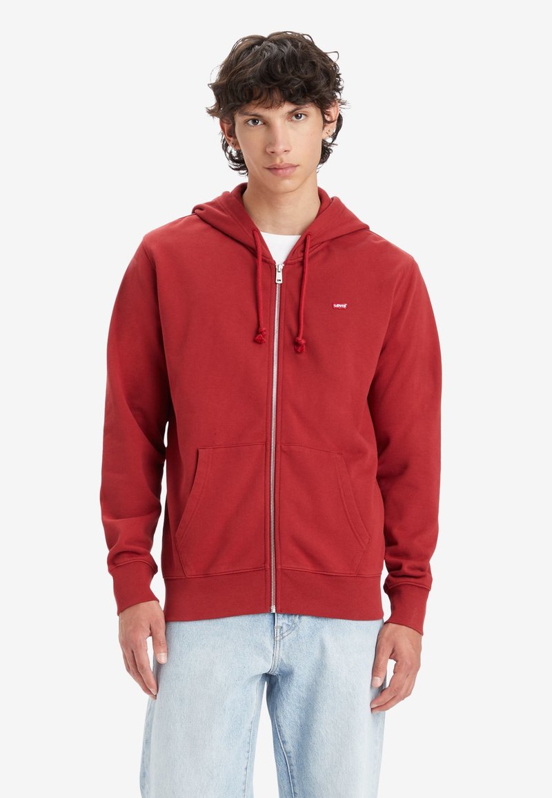 Felpa rossa con zip in cotone, con cappuccio foderato, lacci e tasche anteriori. Logo bianco sul lato sinistro del petto. Tessuto morbido.