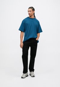 Tirkīza krāsas īsām piedurknēm T-krekls ar apaļu kaklu un Nike logotipu, apvienots ar melniem biksēm un pelēkiem sporta apaviem. Vienkāršs, brīvs piegriezums.