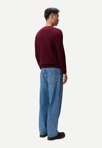 Vinröd stickad tröja med rund hals, kombinerad med ljusblå jeans med lös passform och bruna skor. Texturen verkar mjuk och mysig.