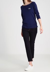 Navyblå långärmad skjorta med "Polo" broderat, tillsammans med mörka jeans och vita sneakers. Mjuk textur och avslappnad passform.