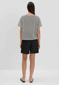 Zwart-wit gestreepte korte mouwen shirt met een ontspannen pasvorm, gecombineerd met zwarte shorts en gedragen met platte sandalen. Effen achtergrond.