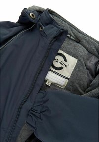 Marineblauwe jas met een zachte grijze fleece binnenkant, voorzien van een rits, drukknoopjes en een label aan de binnenkant. Textuurmaterialen en aangesloten manchetten.