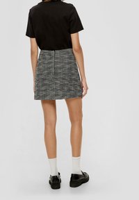 Černý top s krátkým rukávem v kombinaci s texturovanou, vysoce pasovanou sukní v černé a bílé barvě, doplněný černými botami a bílými ponožkami.