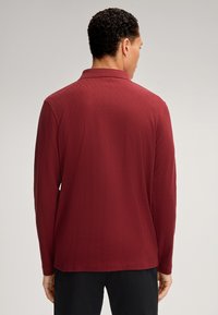 Polo a maniche lunghe color bordeaux con motivo a diamante testurizzato, dotato di colletto e orlo dritto. Realizzato in tessuto leggero.