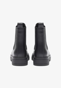Botas de tobillo de cuero negro con un acabado suave, paneles laterales elásticos y suelas de goma gruesas y texturizadas. Diseño minimalista, sin herrajes visibles.