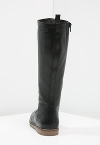 Bota de cuero negro hasta la rodilla con una textura suave, un leve tacón, cremallera trasera y una tela en la parte superior. Detalle de costura sutil visible.