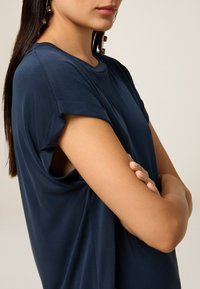 Top corto blu navy con maniche arrotolate e vestibilità rilassata. Tessuto morbido con una superficie liscia, caratterizzato da un design aperto sotto le braccia.
