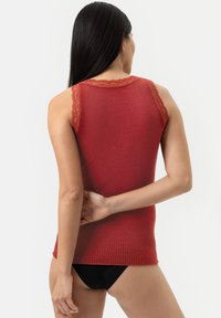 Débardeur rouge à côtes avec une finition en dentelle au niveau du col et des épaules. Le tissu est texturé avec un design ajusté. Bas noir visible.