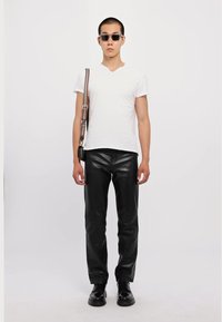 Witte T-shirt met korte mouwen, strakke zwarte leren broek, zwarte schoenen en een zonnebril. Een schoudertas hangt van de schouder.