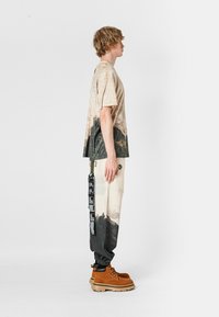 Camiseta en crema con estampado de naturaleza; pantalones jogger negros con detalles gráficos y puños elásticos; botas marrones con suela gruesa.