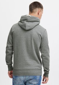 Sudadera gris con un acabado texturizado, con capucha ajustable y puños y dobladillo acanalados. La vista trasera revela un diseño minimalista sin gráficos.