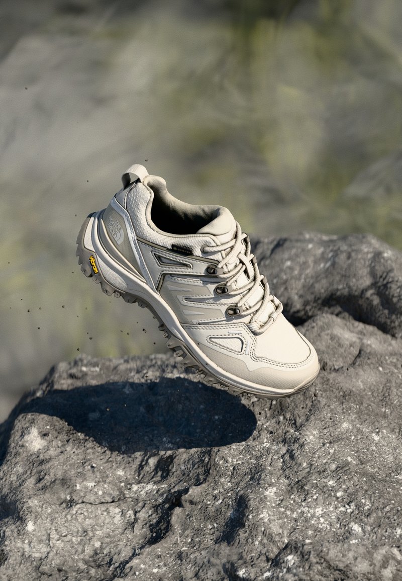 Light beige hiking shoe, made from leather and mesh. Features a textured sole, laces, and prominent side patterns. Vibram logo on heel.