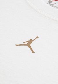 Pruun merevaik korvpallimängija hüppamas ühe käega palli haarates valgel kangal kaeluse lähedal.