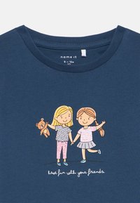 Námornícka modrá bavlnená tričko s grafickým motívom dvoch detí, ktoré sa držia za ruky, jedno s teddy medvedíkom, a textom "zabávaj sa so svojimi priateľmi."