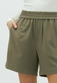 Khaki šortky s elastickým pasem a bočními kapsami, které mají jemnou, hladkou texturu a rovný střih.