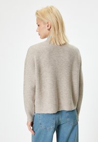 Jasno beżowy sweter o prążkowanej fakturze z wysokim kołnierzem i luźnym krojem, zestawiony z niebieskimi spodniami o szerokich nogawkach. Miękka tekstura, casualowy styl.