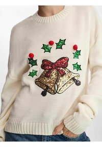 Kremowy sweter dziany z świątecznym wzorem dwóch dzwonków z złotych cekinów, czerwonej kokardki, zielonych liści ostrokrzewu i czerwonych pomponów.