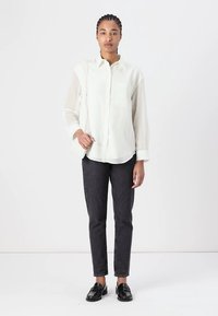 Hvit skjorte med gjennomskinnelige ermer, kombinert med mørke slim-fit jeans og svarte loafers. Enkel, klassisk design uten synlige mønstre.