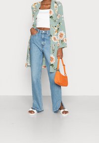 Kimono floral verde claro, top corto blanco, jeans azules de cintura alta con aberturas laterales, sandalias blancas y bolso naranja con textura.