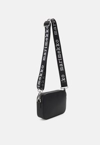 Borsa rettangolare nera con una superficie liscia e una chiusura a zip. Presenta una tracolla a motivo bianco e nero con il testo "marimekko".