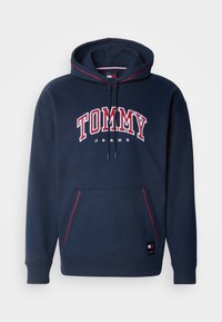 Námořnická mikina s kapucí a červenobílým nápisem "TOMMY JEANS", šňůrková kapuce, přední kapsa a červené kontrastní švy. Směs bavlny.