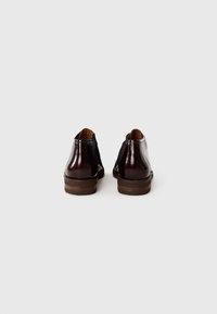 Braune Leder-Ankle-Boots mit einem glänzenden Finish, ausgestattet mit einem niedrigen Absatz und elastischen Seitenpaneelen für einfaches An- und Ausziehen. Klassisches Design mit geschwungenem Schaft.
