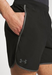 Pantalones cortos deportivos negros con una cinturilla gris, que cuentan con un bolsillo lateral y un pequeño logotipo gris en la parte inferior de la pierna. Textura de tela suave.