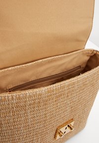 Borsa a tracolla in paglia intrecciata con interno in tessuto beige, pattina aperta, tasca interna con zip e chiusura a fibbia rettangolare color oro.