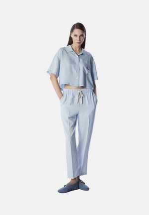 Camisa de botón corta de color azul claro, con mangas cortas y bolsillo en el parche, combinada con pantalones holgados a juego y cómodas zapatillas azules.