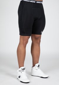Zwarte sportshorts met een getailleerd ontwerp en een elastische tailleband, voorzien van "GORILLA WEAR" branding. Gecombineerd met witte hoge sneakers.