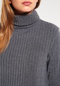 Maglione grigio a coste con collo alto, caratterizzato da una texture morbida e maniche lunghe. La vista ravvicinata mette in evidenza il motivo a maglia.