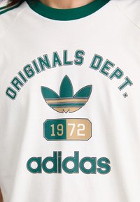 White t-shirt with green and gold graphic print. Features "ORIGINALS DEPT." text, a stylized three-leaf logo, and "1972" below the logo.