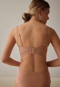 Lys rosa bikinitop med justerbare stropper og en hægte lukning bagpå. Glat tekstur og minimalistisk design.
