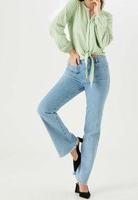 Jasnozielona koszula zapinana na guziki z wiązaniem w talii, do tego jasno-niebieskie jeansy z rozszerzanymi nogawkami oraz czarne buty na obcasie, z surowym wykończeniem na dole.