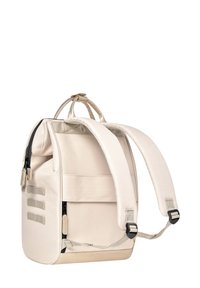 Sac à dos beige avec des bretelles rembourrées, en tissu texturé, double poignée supérieure, fermeture éclair, et sangles d'accent horizontal.