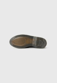 Suola di sneakers nere con una superficie in gomma testurizzata, caratterizzata da un battistrada a motivo per una migliore aderenza e un aspetto leggermente usurato.