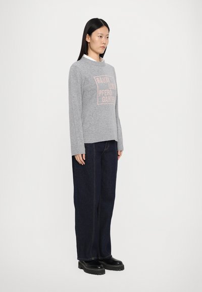 Maglione grigio con una grafica testuale rosa sul davanti, abbinato a jeans a gamba larga blu scuro e stivaletti neri con plateau. Dettaglio del colletto semplice.