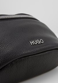 Pochette in pelle nera texture con zip argento e logo del brand "HUGO" argento sul fronte.