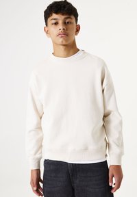 Lichtbeige sweatshirt van zacht materiaal, met een ronde halslijn, lange mouwen en geribbelde manchetten. Gemaakt in combinatie met donkere jeans.