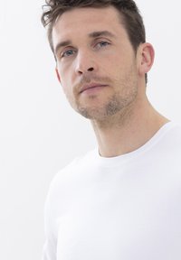 Witte T-shirt met ronde hals van katoen, met een gladde textuur. Het model heeft kort, tousled haar en een lichte stoppelbaard.