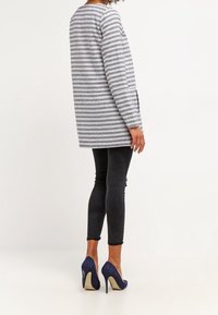 Maglietta a maniche lunghe a righe in grigio e blu navy, abbinata a jeans skinny neri e tacchi alti blu. Presenta un taglio dritto e vestibilità rilassata.